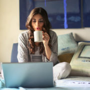 Canva Woman in Grey Jacket Sits on Bed Uses Grey Laptop
