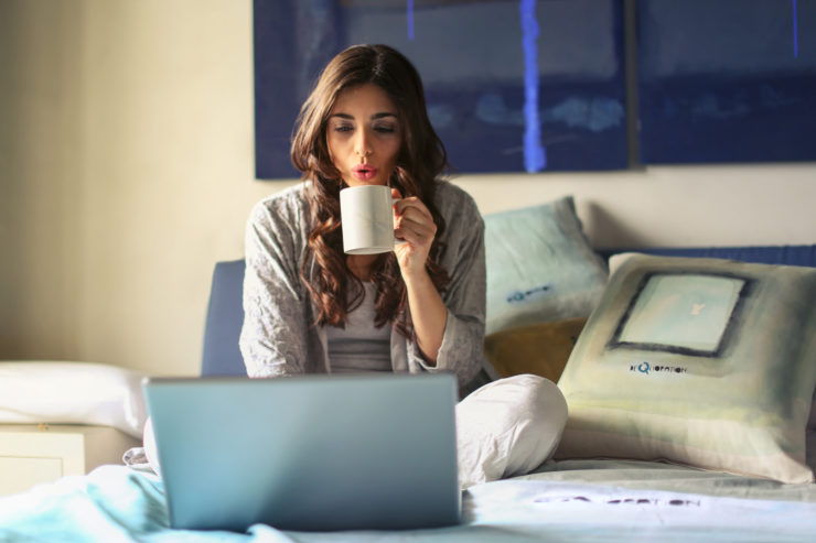 Canva Woman in Grey Jacket Sits on Bed Uses Grey Laptop