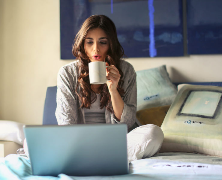 Canva Woman in Grey Jacket Sits on Bed Uses Grey Laptop