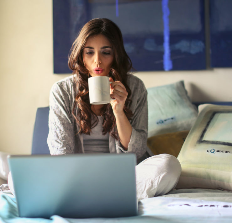 Canva Woman in Grey Jacket Sits on Bed Uses Grey Laptop